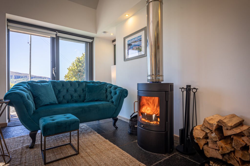 A warm cosy fireplace and jewel blue sofa in the living room of the Byre, a two-person Skye and Shore studio property