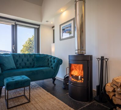 A warm cosy fireplace and jewel blue sofa in the living room of the Byre, a two-person Skye and Shore studio property