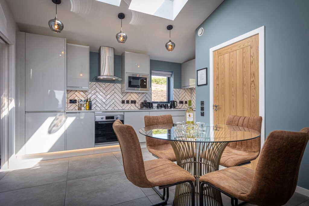 The dining and kitchen area at Tidal Reach, with brown leather dining chairs and a designer glass table