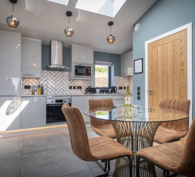 The dining and kitchen area at Tidal Reach, with brown leather dining chairs and a designer glass table