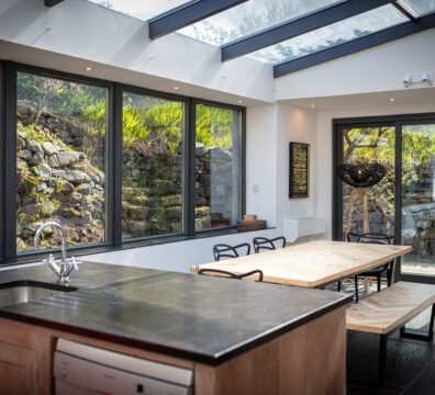 Tern House kitchen, with black granite worktops, a light wood herringbone dining table and designer chairs