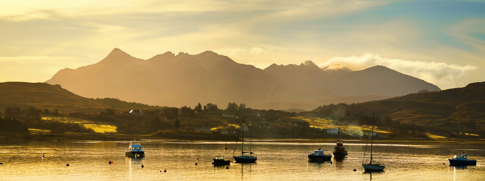 The Cuillin mountains of Skye viewed at sunset over a serene Portree harbour